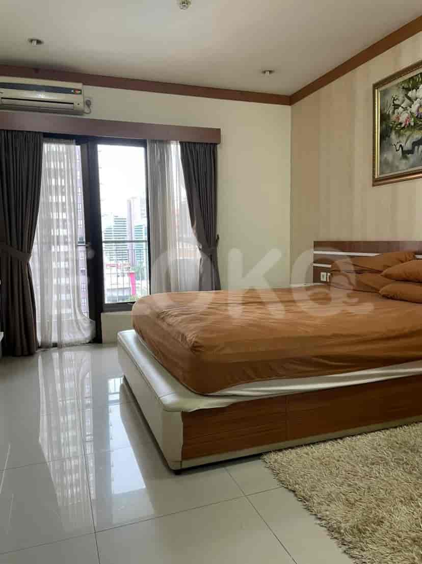 A spacious bedroom with a large window, a king-sized bed, and drapes.