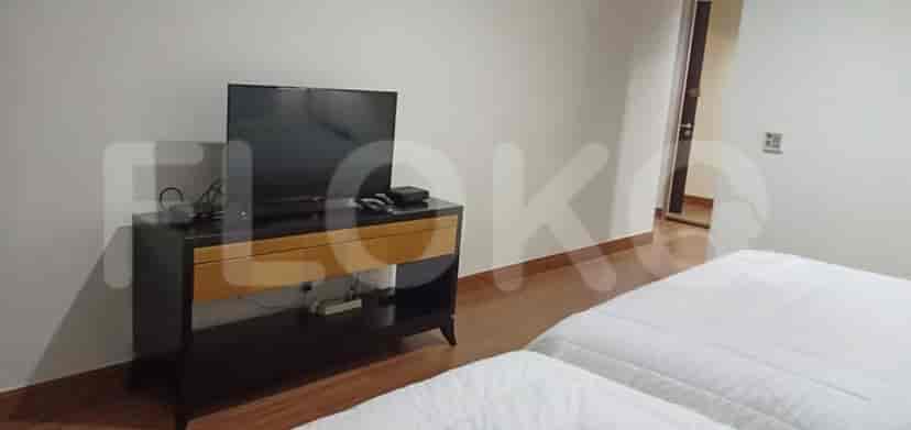 A modern bedroom with two twin beds, a TV on a wooden stand, and a door leading to a hallway.