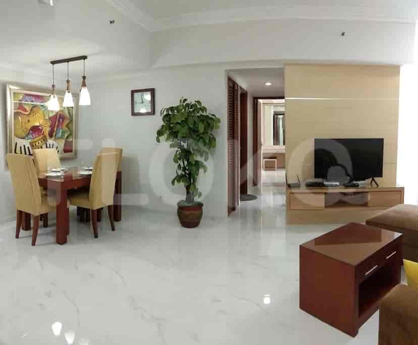 Area ruang tamu dan ruang makan modern dengan meja makan, seni dinding, dan pemandangan dapur.