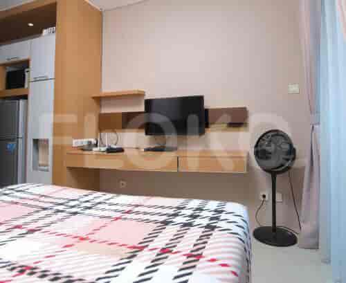A modern bedroom with a tv mounted on the wall, a bed with a checkered bedspread, and a standing fan.