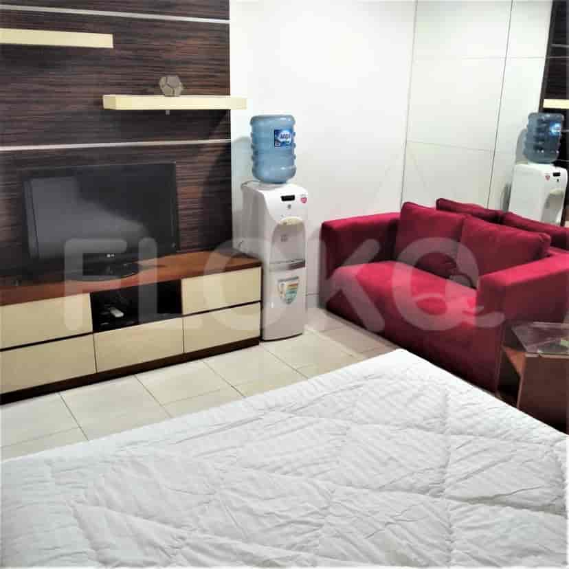 A combined living and dining area, showcasing a compact layout with a red sofa, TV, and a water dispenser.