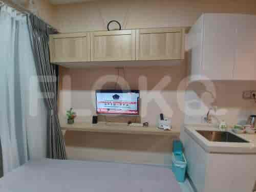 A combined kitchenette and bedroom area with a TV, cabinets, and bed.