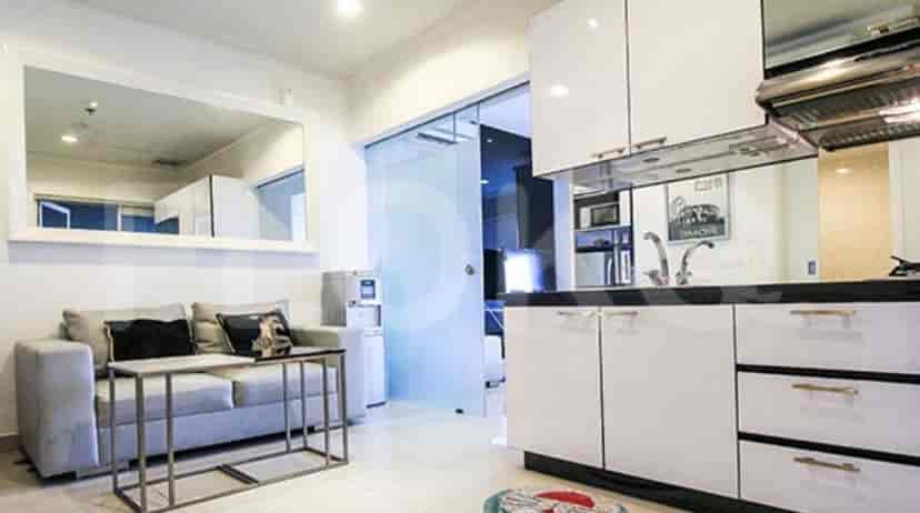 A combination living room and kitchen area with a grey sofa, and white kitchen cabinets.