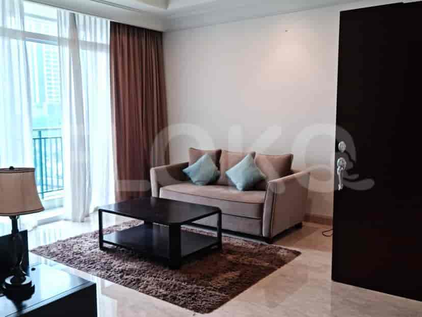 A cozy living room featuring a beige sofa with teal cushions, a dark coffee table on a brown rug, and large windows with brown and white curtains.