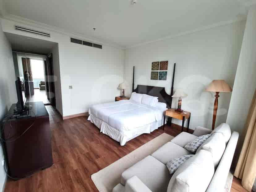 A spacious bedroom with a king-size bed, wooden flooring, a seating area with a sofa, and bedside tables with lamps.