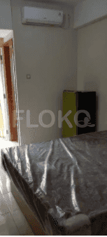 A small bedroom with a bed, air conditioning, and a refrigerator.