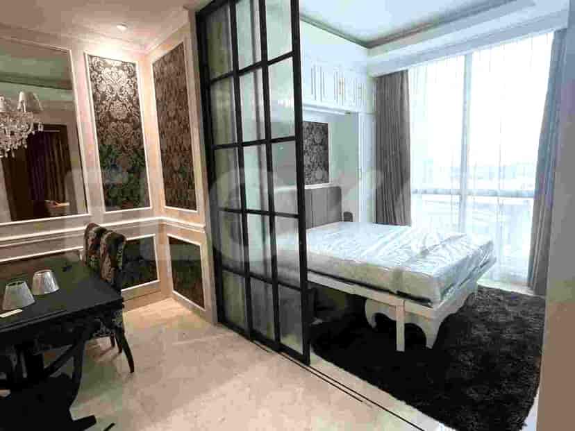 A room divider with black framed glass panels, separating a dining area from a living space, featuring a dining table with chairs and a glimpse of a sofa.