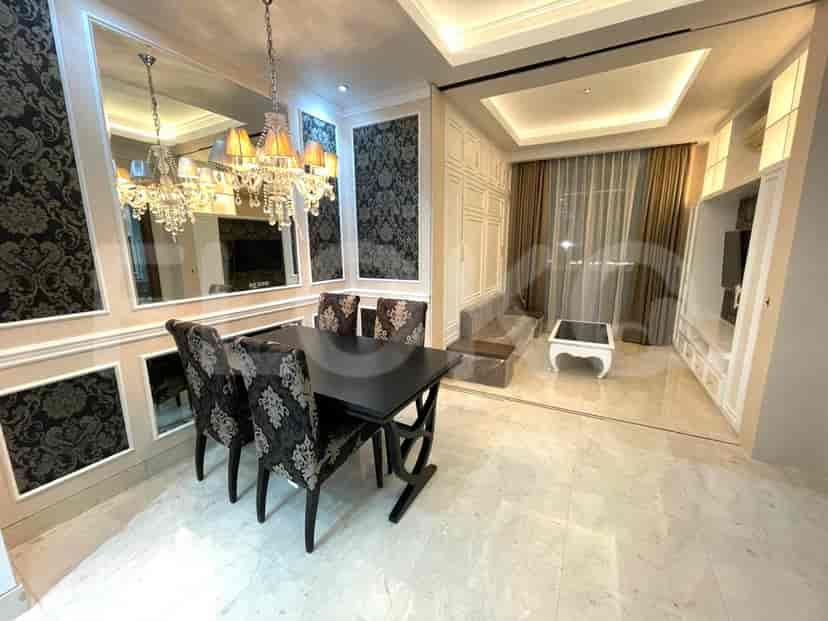An open-plan living and dining area with a dark dining table, a plush sofa, a coffee table, and ornate wall paneling and chandeliers.