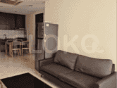A combined living room and kitchen featuring a dark brown sofa, a fridge, a dining table with chairs, and a kitchen area.