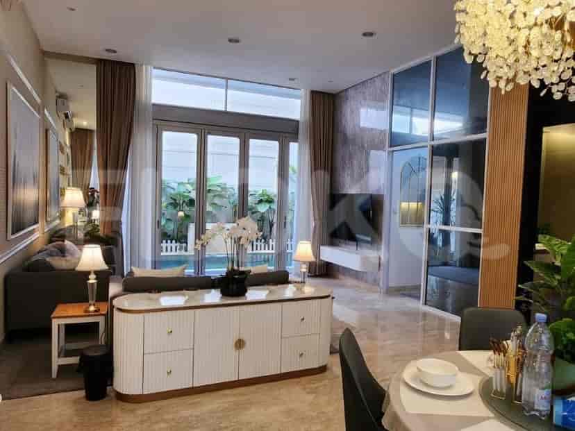 A modern living room with large windows overlooking an outdoor garden, a white cabinet, and a chandelier.