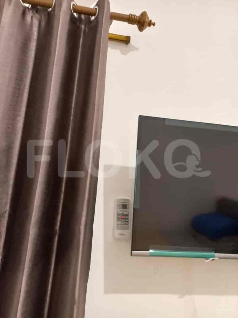 Close-up of a wall-mounted TV, with the remote and curtains visible.