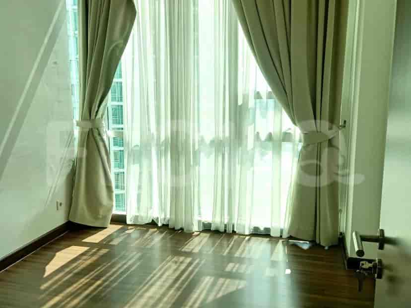 Bedroom with large windows and dark wood flooring, beige curtains and white walls.