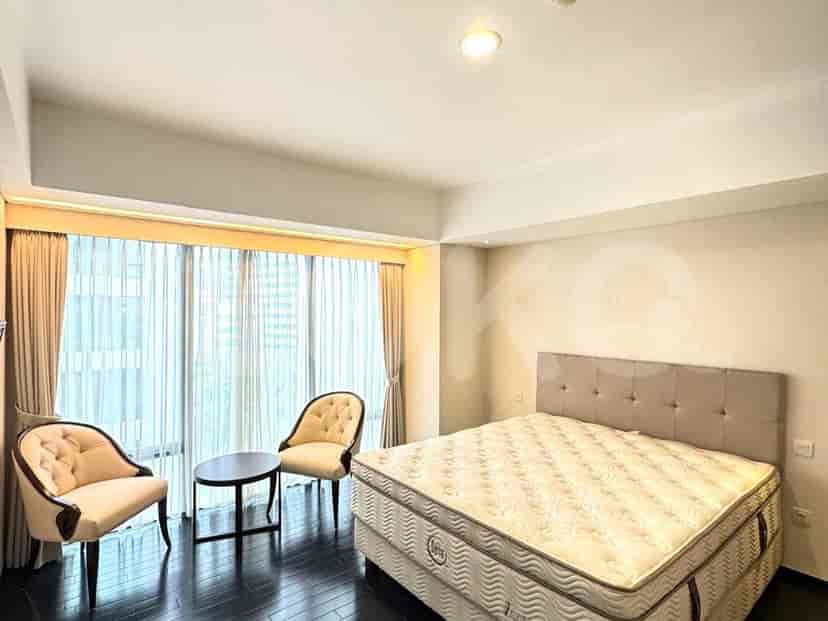 Kamar tidur cerah dengan tempat tidur ganda, meja samping tempat tidur, dan area tempat duduk dengan jendela besar yang memberikan pemandangan.