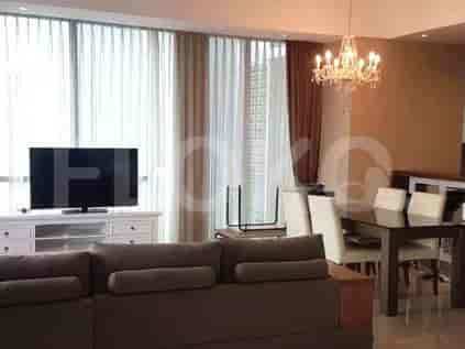 A modern living room with a brown sofa, TV, and dining area, featuring large windows with sheer curtains.