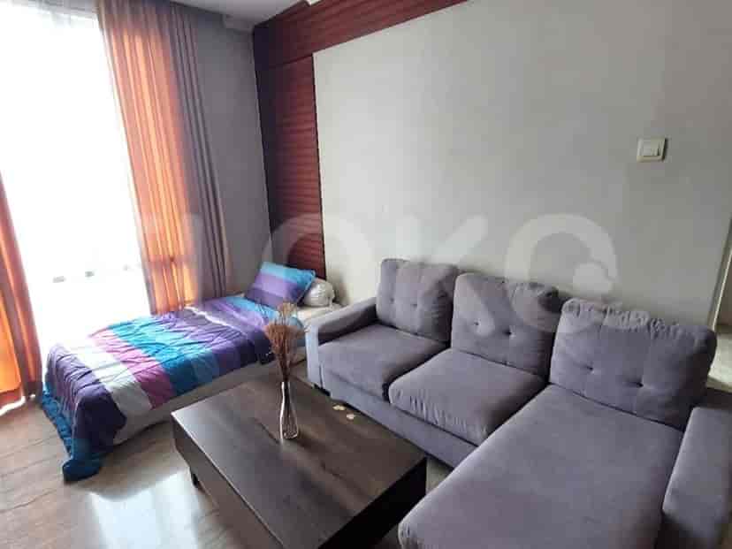 A combined living room and bedroom area, featuring a grey sofa, a single bed, and a coffee table.