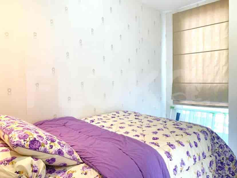 A compact bedroom with a bed, patterned bedding, and a window with a roman shade.