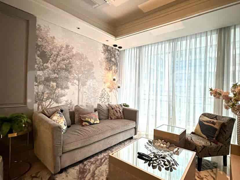 Living room with a grey sofa, patterned accent pillows, tree mural, and glass coffee tables.