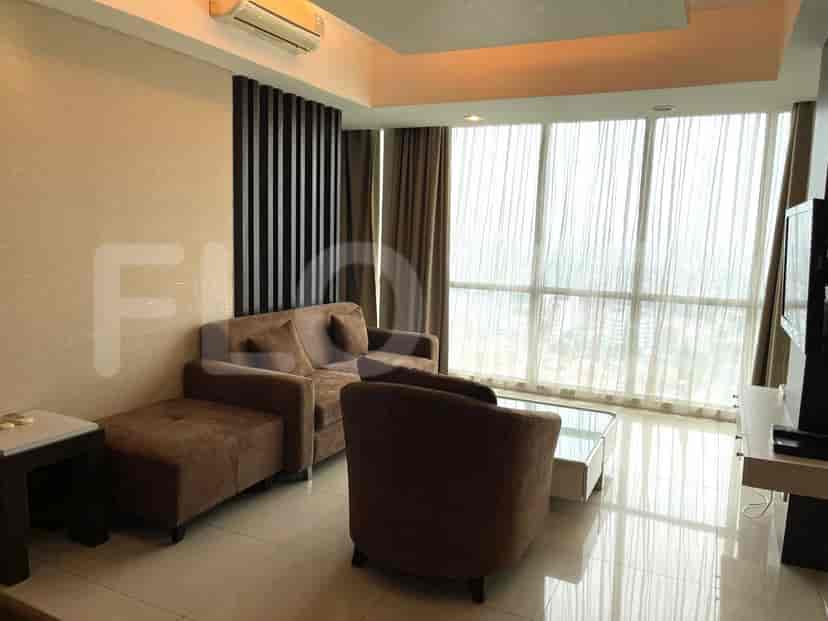A modern living room with a brown sofa, ottoman, armchair, and large windows offering a city view.