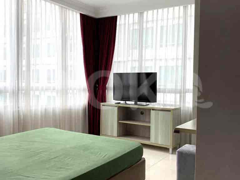 A bedroom with a green-covered bed, a TV, and a window with curtains.
