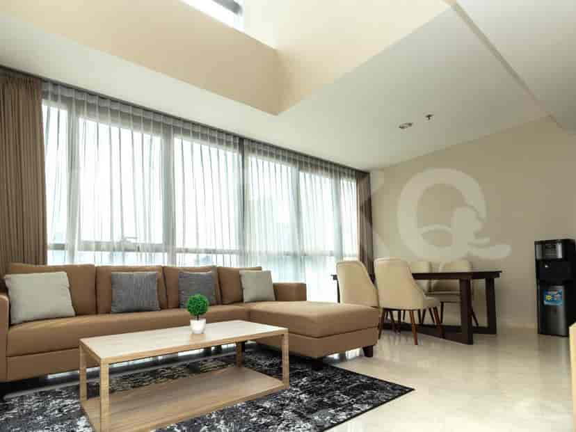 A spacious living room with an L-shaped brown sofa, a wooden coffee table, and a large window with sheer curtains.