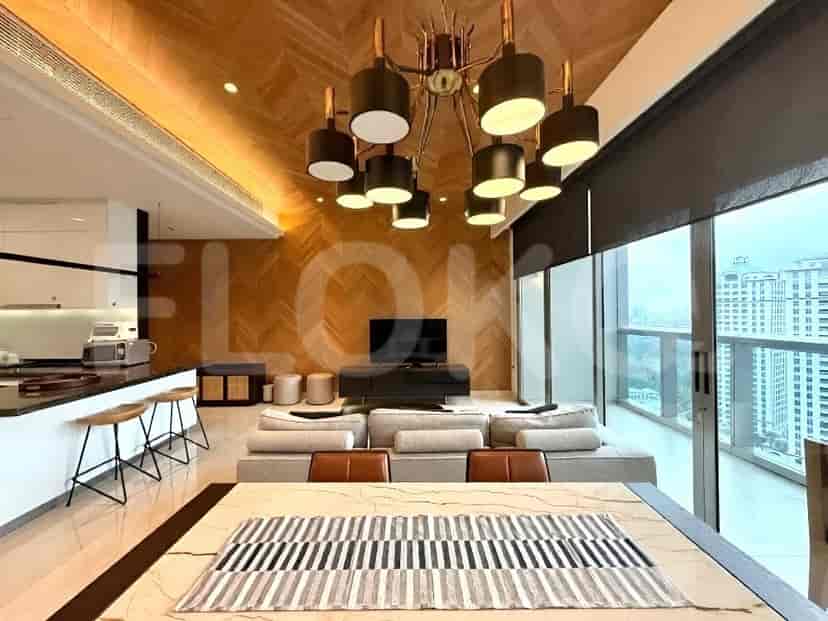 A combined living and dining area with a large dining table in the foreground, a spacious sofa, a wall-mounted TV, and a modern kitchen island.