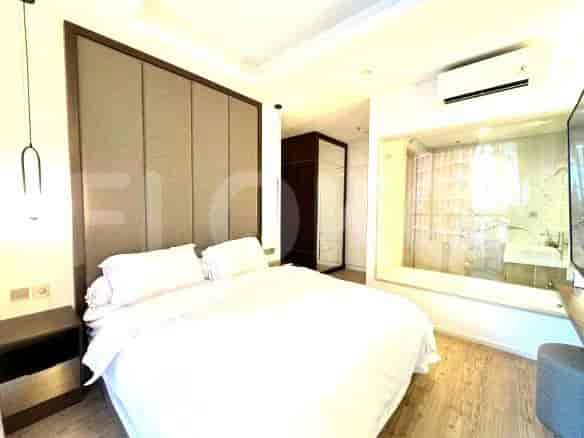 A bedroom with a large bed, headboard, nightstand, and an en-suite bathroom visible through glass.