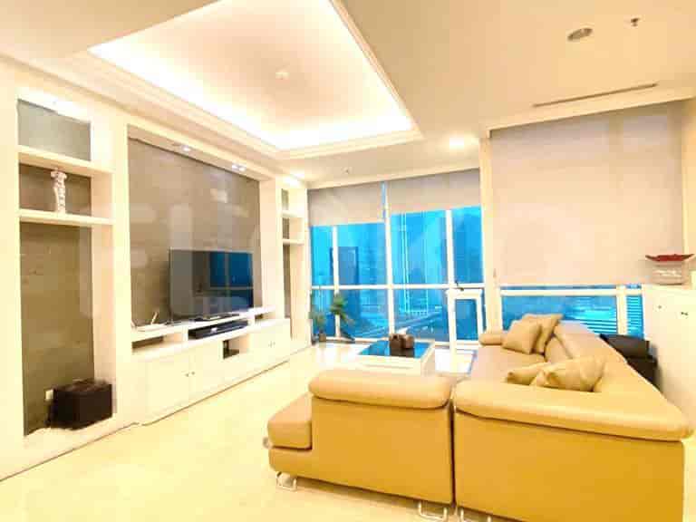 A spacious living room with a large L-shaped sofa, a wall-mounted TV, built-in shelves, and a large window offering a city view.