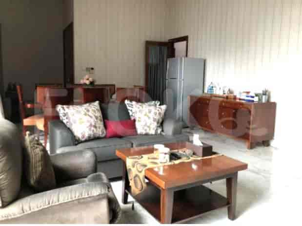 A living room with a dark grey sofa, a coffee table, a wooden cabinet with a refrigerator, and a dining area in the background.