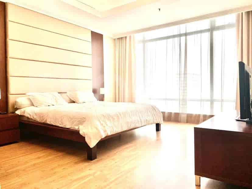 Sebuah kamar tidur dengan ranjang besar, TV, dan jendela dengan tirai.