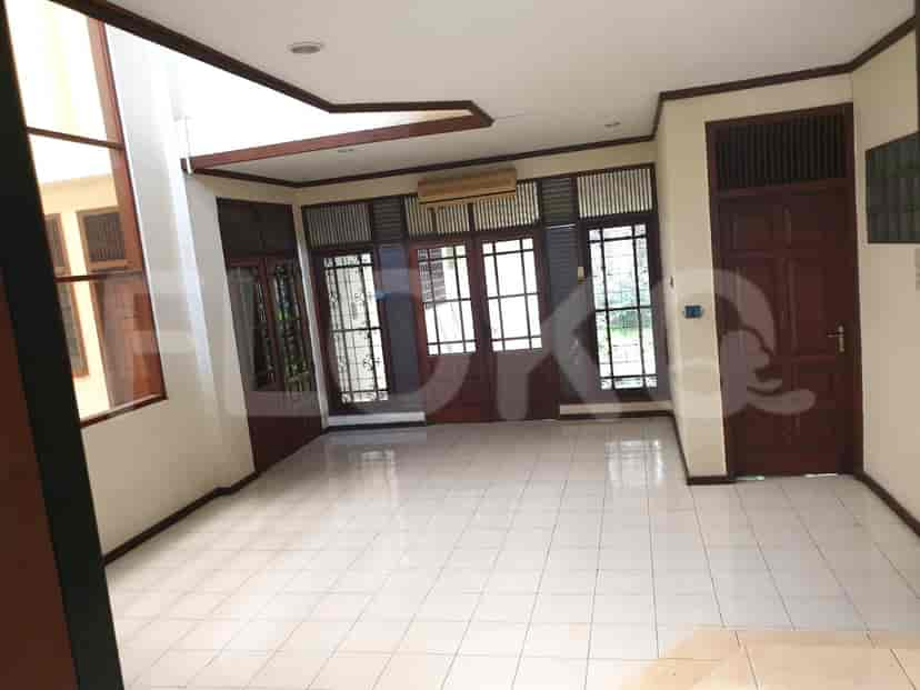 Ruang tamu yang luas dan terang dengan lantai berkeramik, pintu kayu, dan jendela kaca besar.