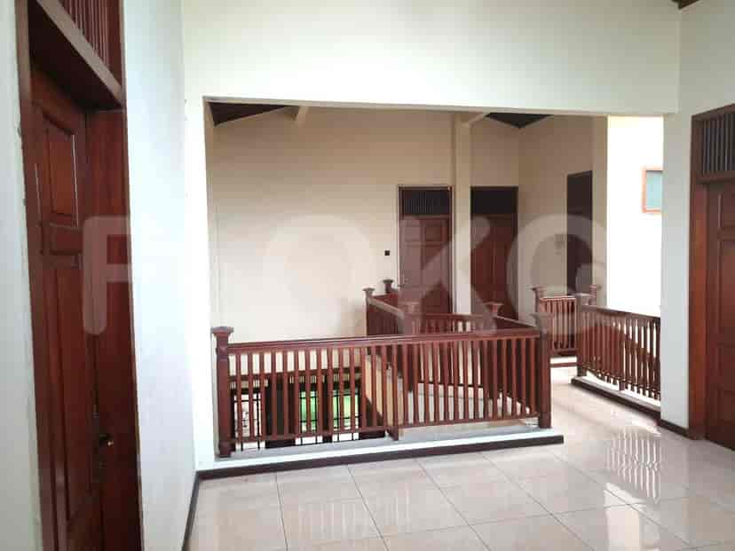 Lorong yang terang dengan lantai berkeramik, pintu kayu, dan pagar kayu yang menghadap ke lantai bawah.