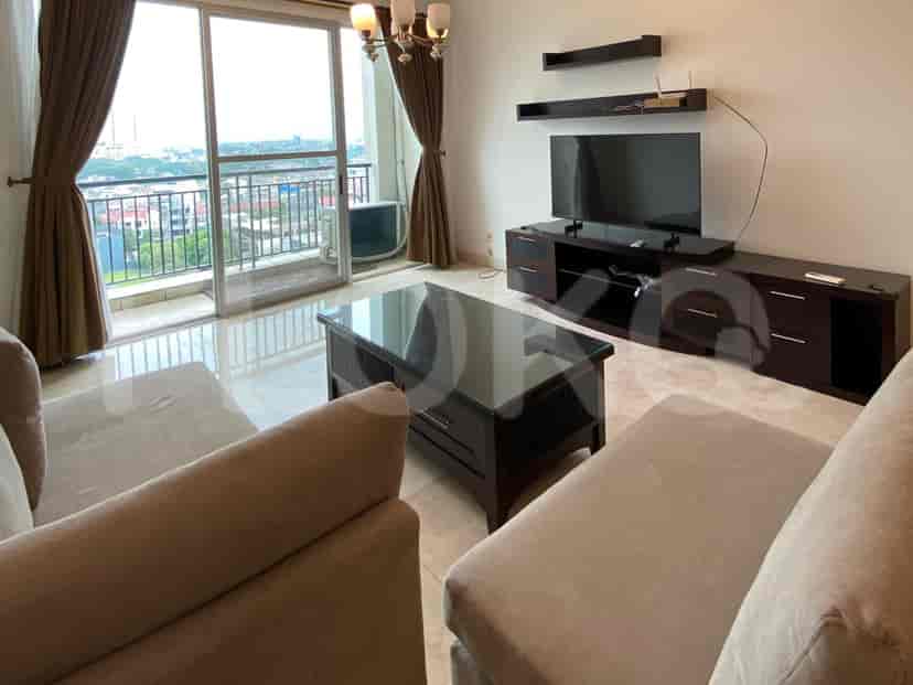 A spacious living room with an L-shaped grey sofa, wall-mounted smart TV, and large window with sheer curtains.
