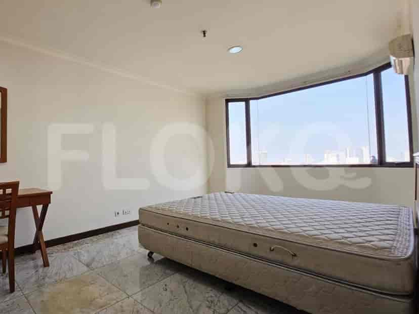 A bedroom with a large bed, a desk, and a bay window offering a city view.