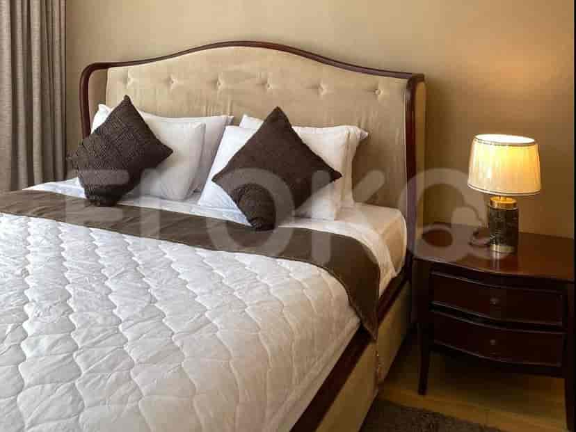 Kamar tidur utama menampilkan tempat tidur besar dengan headboard berumbai dan meja nakas dengan lampu.