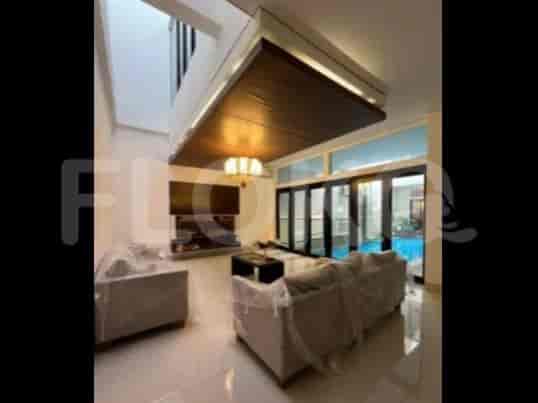 A spacious living room with an L-shaped grey sofa, wall-mounted smart TV, and large window with sheer curtains.