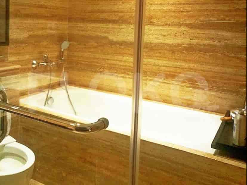 A bathroom with a bathtub, marble-patterned walls, and glass enclosure.