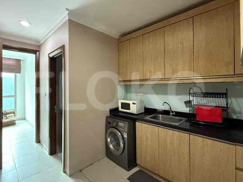 A compact kitchen with light wood cabinets, a black countertop, sink, microwave, and washing machine.