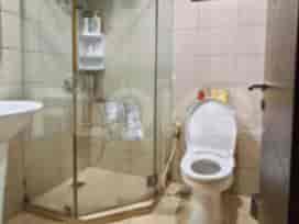 Kamar mandi dengan shower kaca, toilet, dan wastafel.