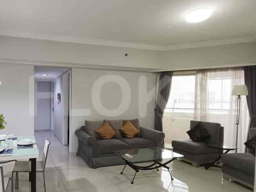 A well-lit living room with grey furniture, glass coffee table, and access to a dining area and balcony.