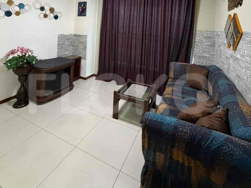 Sebuah ruang tamu dengan sofa berpola, meja kopi, rak televisi, dan dekorasi bunga di dinding.