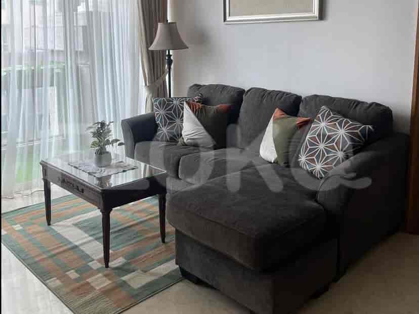 A spacious living room with a dark grey sectional sofa, a glass-top coffee table, and sheer curtains.
