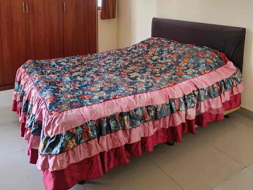 Bedroom with a single bed dressed in a floral comforter and ruffled pink and dark red bed skirt.
