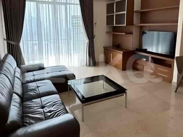 A modern living room with a black leather sectional sofa, a glass coffee table, and a large window with sheer and dark curtains.
