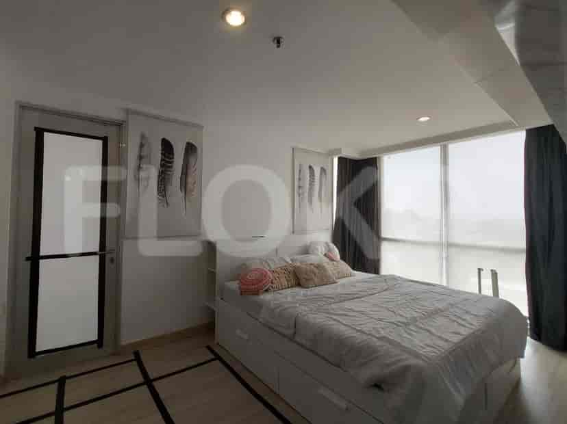 A bedroom with a large bed, white storage drawers, large windows with dark curtains, and feather-themed artwork.