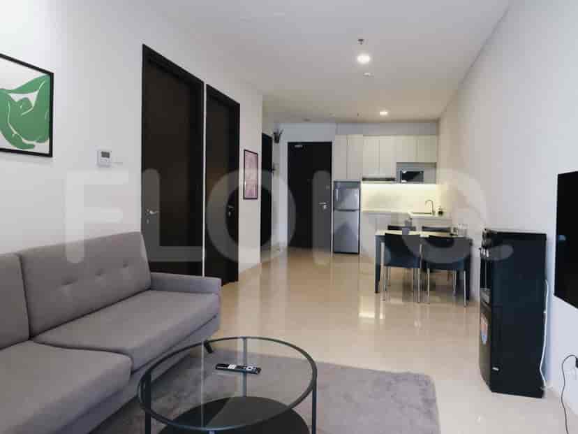 A combined living area and kitchenette with a grey sofa, glass coffee table, and a compact kitchen with stainless steel appliances.