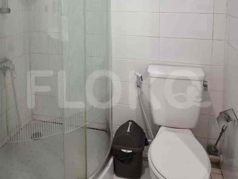 A compact bathroom with a toilet, a shower stall, and a trash bin.