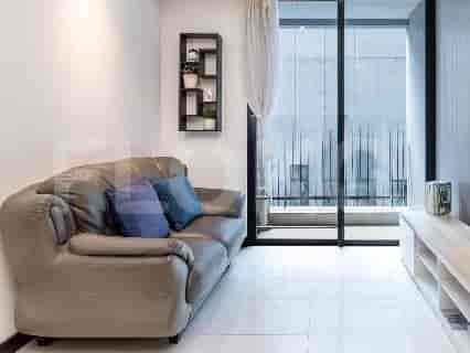 Ruang tamu yang nyaman dengan sofa kulit abu-abu, rak dinding dekoratif, dan pintu kaca besar menuju balkon.