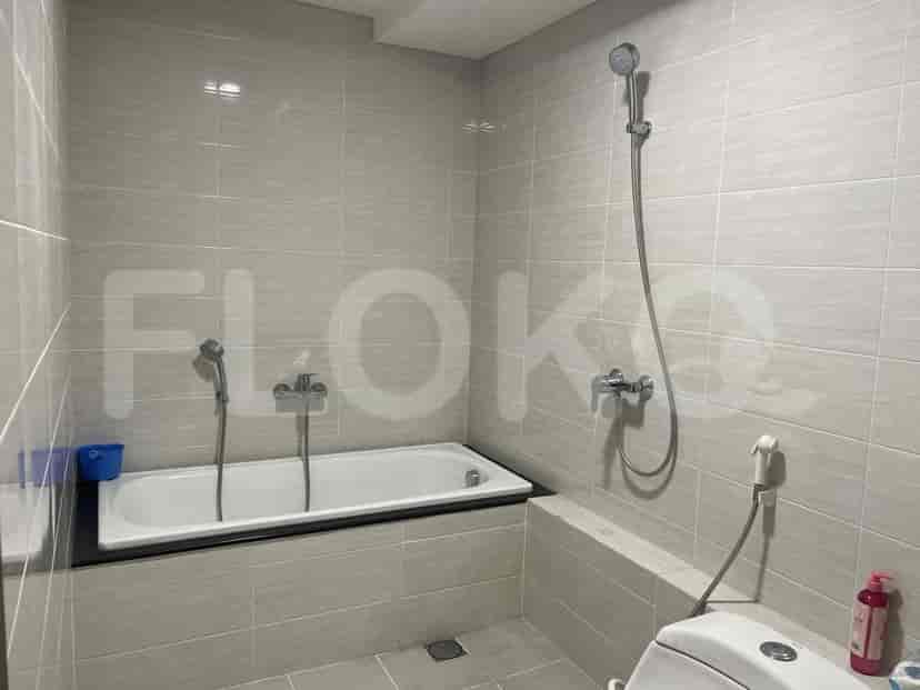 A bathroom with light grey tiled walls, a bathtub, a toilet, and a showerhead.