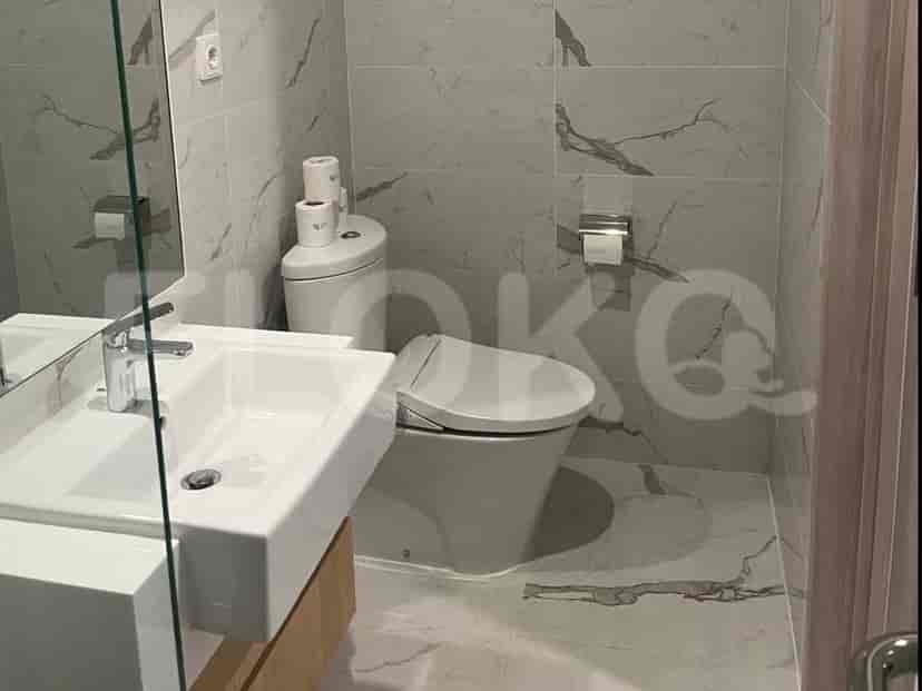 A modern bathroom with a sink, toilet, and marble-tiled walls.