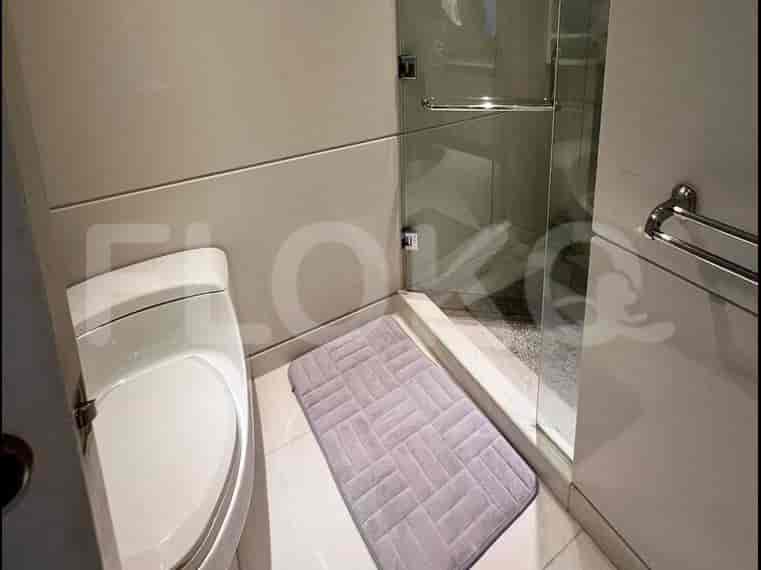 Kamar mandi modern dengan pancuran kaca, toilet putih, dan karpet kecil.